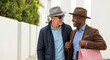 © Inspire Shots Hub - Two men in stylish hats and smart casual attire converse outdoors, one carrying shopping bags, symbolizing friendship, leisure, and modern shopping.