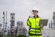 © VStudio - Professional male industrial engineer speaking on walkie talkie holding laptop reporting at petrochemical refinery plant for sustainable corporate oil and gas manufacturing business management.
