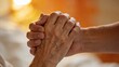 © Husen - Two people hold hands in a warm and comforting gesture of support and love indoors.