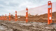 © CK Studio - Construction site with orange safety fence along muddy ground, heavy machinery in background for development projects.