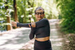 © standret - Mature woman in black athletic wear stretches her arm while standing on a tree-lined path, showcasing a healthy lifestyle in a natural outdoor setting