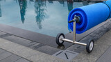 Blue solar pool cover on a roller with wheels next to a swimming pool