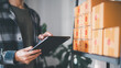 © chaylek - Inventory manager checking ecommerce stock and package organization using tablet in warehouse workspace, supporting logistics management, order tracking, and retail inventory operations.