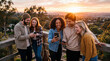 © MystoganCreative - A diverse group of happy young friends laughing and looking at their smartphones together on a scenic outdoor deck at sunset.