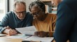 © miss irine - Elderly couple reviews financial documents with consultant. Man signs paper, woman reads contract at table. They discuss pension and savings for future.