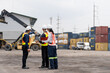 © Supachai - Logistics team discussing operations pointing at cargo containers in shipping port yard. Group of industrial supervisors wearing safety helmets and vests using digital tablet at warehouse terminal