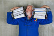 © BIB-Bilder - Stressed senior craftsman carrying heavy folders, symbolizing excessive bureaucracy, paperwork overload and administrative pressure on small business and trades in Germany and Europe.