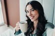 © deagreez - Smiling woman holding a coffee mug in a cozy morning selfie portrait, relaxed at home and enjoying a warm beverage
