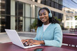 © ADDICTIVE STOCK - Young African woman with headphones using laptop outdoors