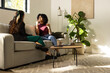 © Wavebreak Media - Diverse female friends talking on sofa in living room with laptop, mug, burgundy top, blazer
