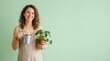 © spyrakot - Woman holding watering can and potted plant against pastel green wall