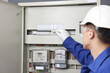 © New Africa - Electrician checking fuse box with electrical meters indoors