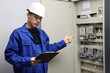 © New Africa - Electrician with clipboard checking electrical meters in fuse box indoors