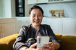 © Davor - Smiling woman using smartphone at home on sofa