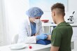 © New Africa - Nurse drawing blood sample of patient's vein with syringe at white table in clinic
