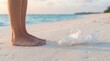 © 5 Grace Media - Barefoot person standing on sandy beach next to discarded plastic bottle, highlighting environmental pollution and ocean waste.