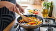 © Miravo - Person cooking fresh vegetables in a frying pan on a stovetop.