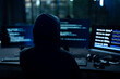 © Velocitystock777 - Male computer hacker in black hoodie typing code on computer in a dark room with light reflection on glasses.