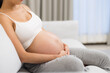 © leungchopan - Pregnant woman resting on sofa gently holding her belly at home