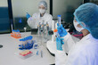 © NINENII - Asian women team researchers examining natural water sample for contaminants and microplastics next to laboratory bottle.