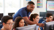 © Aurora Aesthetics - african american male technology teacher middle school computers coding stem classroom diverse tech instructor pointing out programming details on screen to attentive young learner in coding classroom
