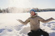 © Johnér - Smiling woman playing with snow while sitting on land at sunny day