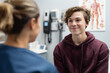 © GraysonStock - Smiling Teen Boy Patient Consulting with Doctor in Clinic Office