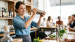 © Xenia - Cheerful female bartender shaking a cocktail behind a wooden bar. Smiling young woman making drinks with fresh ingredients in a lively restaurant