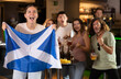 © JackF - Group of friends fans watching match cheering with Scottish flag in bar