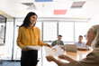 © fizkes - Smiling businesswoman handing out printed materials, presenting business report with financial analysis, statistical charts data to diverse colleagues or clients at collaborative office group meeting
