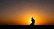 © melisa - Silhouette of a man kneeling in prayer against a vibrant sunset sky