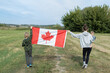 © Anna - An unrecognizable young woman holding a baby and a boy nearby hold a large Canadian flag. Travel, immigration. Happy Canada Day. Pride, a national symbol