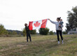 © Anna - young woman and two children hold a large Canadian flag while standing in a park. Travel, immigration. Happy Canada Day. Pride, freedom, a national symbol