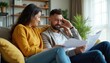 © miss irine - Couple discusses finances at home. Man shows stress over paperwork while woman offers support. They review bills and budget on sofa. Financial planning and empathy.