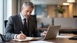 © Eve - Confident senior businessman in formal suit writing notes and using laptop at workspace, legal consulting and corporate executive concept