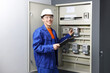 © New Africa - Electrician with clipboard checking electrical meters in fuse box indoors