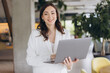 © anatoliycherkas - Professional woman standing, smiling and working on laptop, managing business in a modern office environment