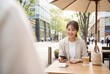 © AdPremium - Smiling young Asian woman using a smartphone for contactless mobile payment at an outdoor cafe terrace in a modern city
