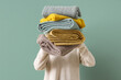 © Pixel-Shot - Young woman with stack of different blankets on turquoise background, closeup