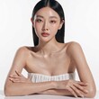 © YoYo & J studio - A young beauty model with long black hair and glowing skin is looking at the camera while sitting with her arms crossed on a white table against a plain white background