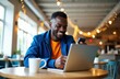 © Vadym - Smiling man works on laptop and phone in cafe. He wears blue jacket and orange shirt. Coffee cup on table. Blurred festive lights background. Modern workspace.