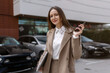 © руслан малыш - Young business woman talking on smartphone near parked cars, holding laptop, waiting and discussing transport or car purchase, urban lifestyle, modern professional scene