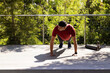 © wavebreak3 - Man performing push-up on wooden deck wearing red athletic shirt dark shorts black shoes smartwatch