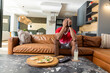 © wavebreak3 - African American adult male sitting on tan sofa covering face wearing red jersey, table with pizza