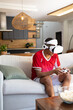 © wavebreak3 - African American man wearing VR headset, red shirt, holding controller on sofa, popcorn, copy space
