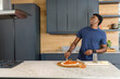 © wavebreak3 - Adult African American man spreading sauce with spoon on pizza dough on wooden peel, copy space