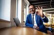 © littlewolf1989 - Businessman making ok gesture with hand, smiling and working on laptop in modern office space