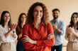 © Pete - Hispanic businesswoman in red shirt smiles with arms crossed. Team in background claps enthusiastically. Success, achievement and positive team spirit shown.