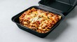 © Alexandre - Lasanha, Black takeout container filled with hot lasagna tomato sauce comfort food