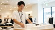 © Musarrof - Smiling young Asian male shop assistant folding white t-shirts on a display table in a modern clothing store.